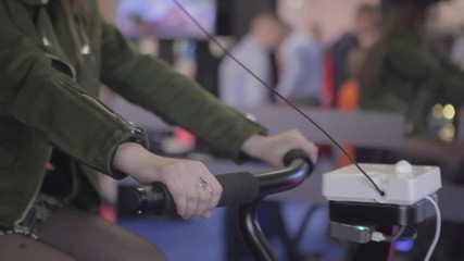 Young girl in virtual reality, rides a bicycle at the exhibition of computer technology. Beautiful young girl playing with vr glasses.  - Powered by Adobe