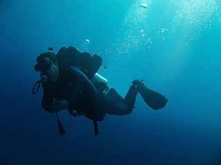 Scuba diver with full equipment is underwater. Sunlight and bubbles.  