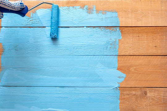 Painting with the paint roller blue color paint on the wooden DIY background for photo