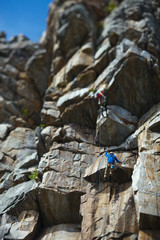 The climber climbs up the rope against the background of a huge rock wall. Two person rope.  Tilt-Shift effect.