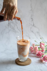 Milk tea. Pouring milk from jar to a cup of ice tea or coffee. Ice tea with carnation on the marble background.