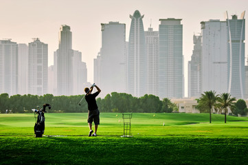 golf player playing golf on the on the grass field against the skyscraper buildings