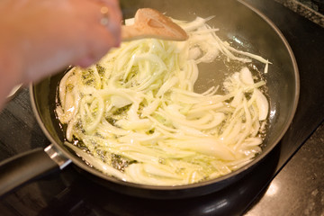 Onions being poached in a pan, and a woman hand moving them with a wooden spoon