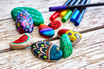Hand-painted colorful pebble stones and acrylic pens on a vintage textured wooden table. Stone...