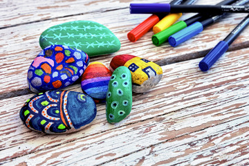 Hand-painted colorful pebble stones and acrylic pens on a vintage textured wooden table. Stone...