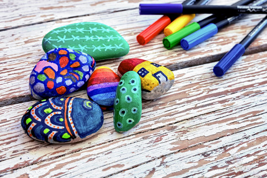 Hand-painted colorful pebble stones and acrylic pens on a vintage textured wooden table. Stone painting.