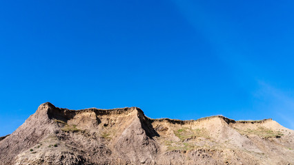 Fototapeta na wymiar Top of a rock and dirt cliff face with a beautiful, vivid blue sky taken at Seaham Hall Beach in County Durham, England on a warm sunny morning.