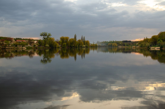 Lake in a village with a reflection of the sky before the rain