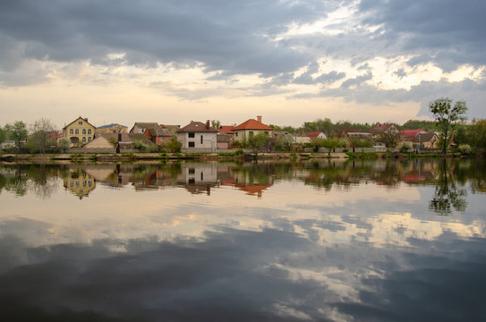 Lake in a village with a reflection of the sky before the rain