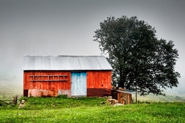 weathered red wooden cottage in a rural area on a cloudy and foggy day