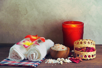 Front view himalayan salt with towel and aroma candle decorate with dry roses on wood table for scrub spa therapy.