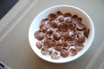 Breakfast Chocolate Cornflakes Cereal with milk in white bowl on the table
