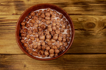 Cereal chocolate balls with milk in a bowl on wooden table. Top view