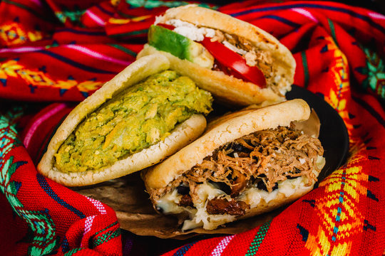 Venezuelan arepas on a colorful background, made with maize and filled with avocado, tomato, meat, cheese and black beans