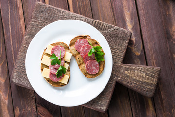 open sandwiches with salami slices rye bread cheese topped parsley on white plate wooden cutting board top view