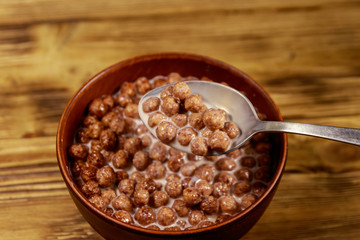 Cereal chocolate balls with milk in a bowl on wooden table. Spoon with breakfast