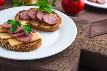 open sandwiches with salami slices rye bread cheese topped parsley on white plate close up