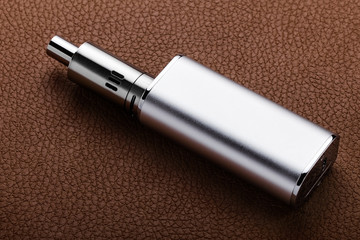 Silver colored electronic cigarette on brown leather background
