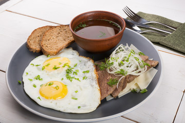 Fried eggs served with bread slices, meat slices and broth