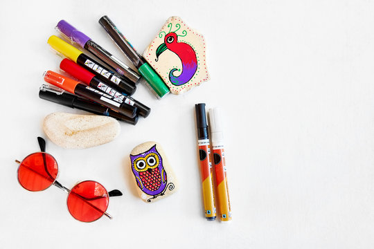 Painted Stones, Acrylic Pens And Sunglasses On A Table With Copy Space. Stone Painting Craft. Flat Lay View.