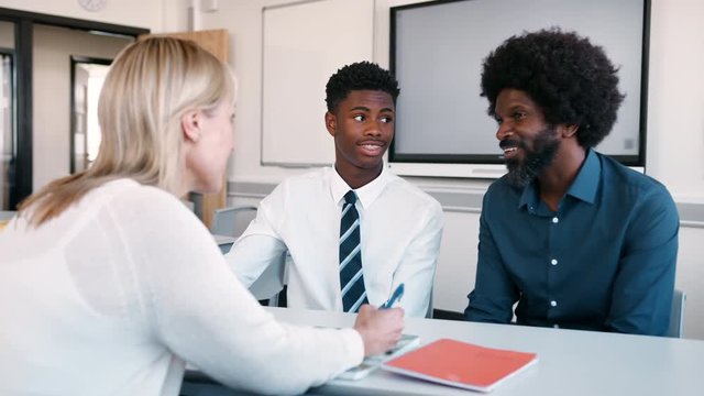 Father And Teenage Son Having Discussion With Female Teacher At High School Parents Evening