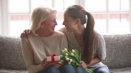 Adult daughter presenting flowers and gift box to old mother - Powered by Adobe