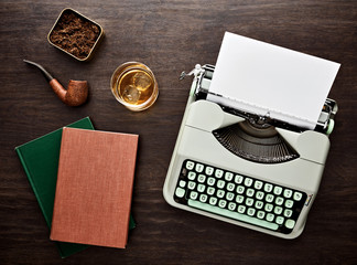 Vintage typewriter, blank paper, pipe, books, tobacco box and a glass of whiskey on the wooden...