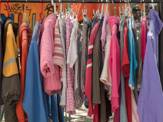 Colourful second-hand clothes and jackets hanging on a rack in a flea market