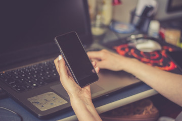 Young woman hand holding a smartphone While typing on a laptop keyboard at home – Person working with multiple devices at the same time – Concept image for multitasking and freelancing