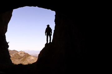 MOUNTAIN MEN ADVENTURER AT THE ENTRANCE OF A LARGE CAVE WITH A MEDIEVAL CASTLE IN THE DISTANCE