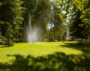 Modern automatic lawn irrigation device in the park. Water is sprayed over lawn grass.