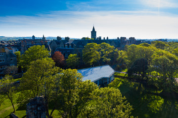 Fototapeta premium A drone shot from the perspective of St Andrews Castle ruins looking towards St Salvator's Quad. Stunning greenery can be seen in the setting sun's light.