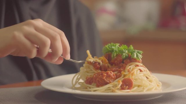 a woman muslimah feed herself a plate of spaghetti served with minced beef and sausage sauce. selective focus