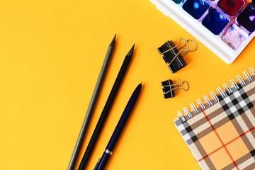 School subjects: pencils, notebook, watercolor paints on a light yellow background. Back to school...