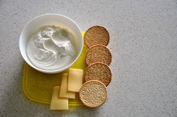 A dish of healthy food. Cottage cheese with cream, hard cheese, galette cookies in a white vase on a yellow stand.