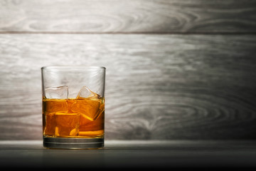 Whiskey glass and ice on wooden bar counter background