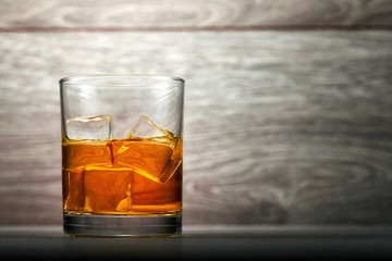 Whiskey glass and ice on wooden bar counter background
