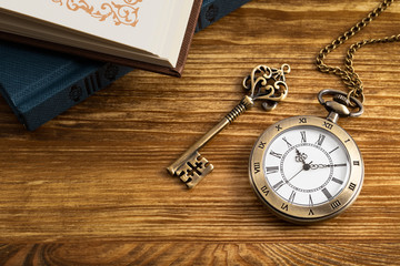 Vintage pocket watch clock with key and book on wooden background