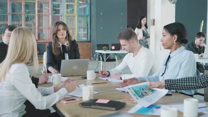 The business team holds a meet up at a large table in the office. One of the staff members gets up and leaves. Creative office interior. Coworking startup team. Office workers