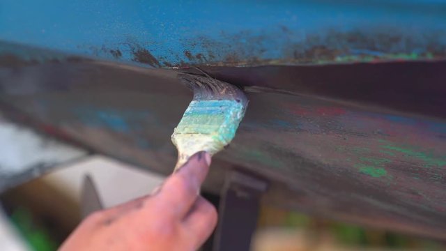 Close up shot of a fisherman painting in slow motion the hull of a boat