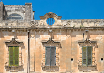 Fachada de piedra, con tres ventanas y contraventanas, de un edificio antiguo el la ciudad de Lecce...