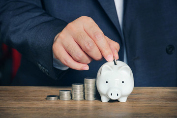 Businessman keep money on piggy saving which decorate with growth coins stack.