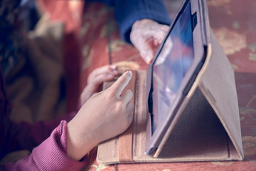 Photograph of the hands of a child and his grandmother using a tablet. Huelva, Spain