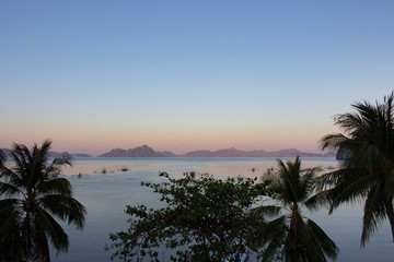 Obraz premium Morning on beach with trees and boats. Sunrise in Palawan, Philippines. Tropical isles in morning dusk with trees on foreground. Asian landscape with traditional philippines boats. Summer vacation.