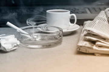 The concept of news. A folded stack of Newspapers on the laptop, a Cup of coffee, a Smoking cigarette in the ashtray. Office worker's Desk.