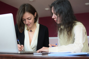 young smartly dressed lady helps another young lady to work with documents, fill forms and sign
