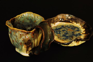 Stylized spectacular clay tea pair of original form decorated with icing on black background. Souvenir products. Play of light and shadow. Concept — style, fantasy, beauty. Selective focus.