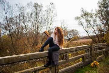 Portrait of young redhead woman in autumn park reading a book