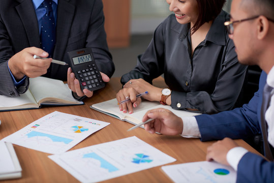 Close-up of businessman showing numbers on calculator to his team while they analyzing financial graphs together at meeting