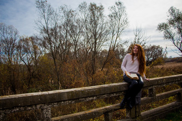 Portrait of young redhead woman in autumn park reading a book